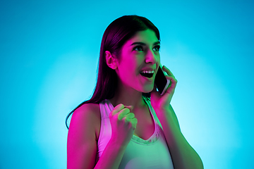 Image showing Brunette beautiful woman\'s portrait isolated on blue studio background in multicolored neon light. Talking phone.