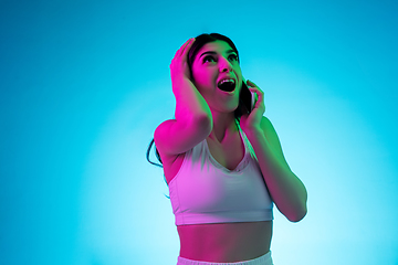 Image showing Brunette beautiful woman\'s portrait isolated on blue studio background in multicolored neon light. Talking phone.