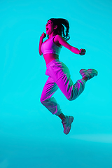 Image showing Brunette beautiful woman\'s portrait isolated on blue studio background in multicolored neon light. Jumping high. flying