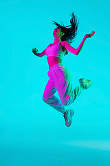 Image showing Brunette beautiful woman\'s portrait isolated on blue studio background in multicolored neon light. Jumping high. flying