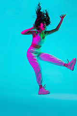 Image showing Brunette beautiful woman\'s portrait isolated on blue studio background in multicolored neon light. Jumping high. flying