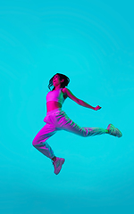 Image showing Brunette beautiful woman\'s portrait isolated on blue studio background in multicolored neon light. Jumping high. flying