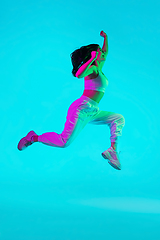 Image showing Brunette beautiful woman\'s portrait isolated on blue studio background in multicolored neon light. Jumping high. flying