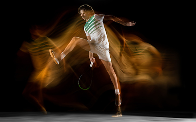 Image showing Young caucasian professional sportsman playing tennis on black background in mixed light