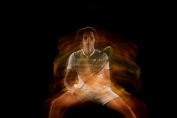 Image showing Young caucasian professional sportsman playing tennis on black background in mixed light