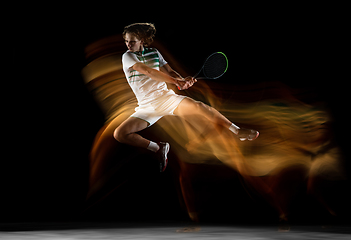 Image showing Young caucasian professional sportsman playing tennis on black background in mixed light