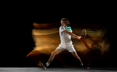 Image showing Young caucasian professional sportsman playing tennis on black background in mixed light