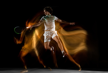 Image showing Young caucasian professional sportsman playing tennis on black background in mixed light