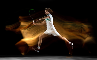 Image showing Young caucasian professional sportsman playing tennis on black background in mixed light