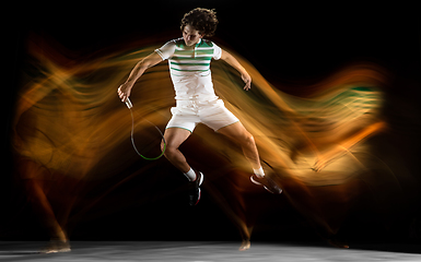 Image showing Young caucasian professional sportsman playing tennis on black background in mixed light