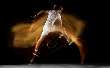 Image showing Young caucasian professional sportsman playing tennis on black background in mixed light