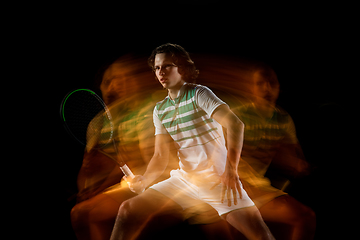 Image showing Young caucasian professional sportsman playing tennis on black background in mixed light