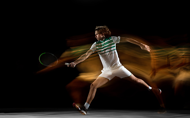 Image showing Young caucasian professional sportsman playing tennis on black background in mixed light