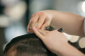 Image showing Close up hands of master barber, stylist does the hairstyle to guy, young man. Professional occupation, male beauty concept