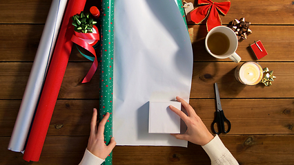 Image showing hands wrapping christmas gift into paper at home