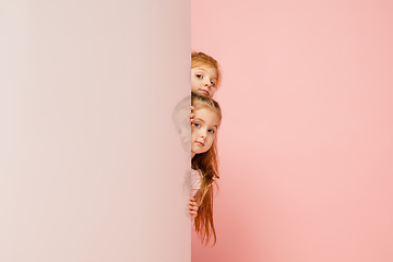 Image showing Happy kids, girls isolated on coral pink studio background. Look happy, cheerful, sincere. Copyspace. Childhood, education, emotions concept