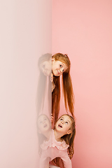 Image showing Happy kids, girls isolated on coral pink studio background. Look happy, cheerful, sincere. Copyspace. Childhood, education, emotions concept