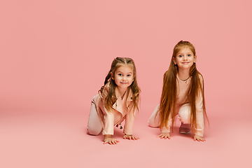 Image showing Happy kids, girls isolated on coral pink studio background. Look happy, cheerful, sincere. Copyspace. Childhood, education, emotions concept