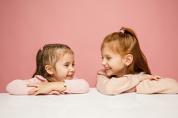 Image showing Happy kids, girls isolated on coral pink studio background. Look happy, cheerful, sincere. Copyspace. Childhood, education, emotions concept