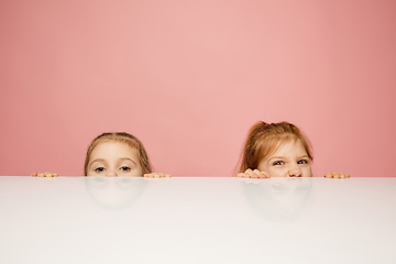 Image showing Happy kids, girls isolated on coral pink studio background. Look happy, cheerful, sincere. Copyspace. Childhood, education, emotions concept