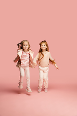 Image showing Happy kids, girls isolated on coral pink studio background. Look happy, cheerful, sincere. Copyspace. Childhood, education, emotions concept