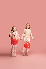 Image showing Happy kids, girls isolated on coral pink studio background. Look happy, cheerful, sincere. Copyspace. Childhood, education, emotions concept