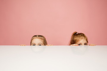 Image showing Happy kids, girls isolated on coral pink studio background. Look happy, cheerful, sincere. Copyspace. Childhood, education, emotions concept