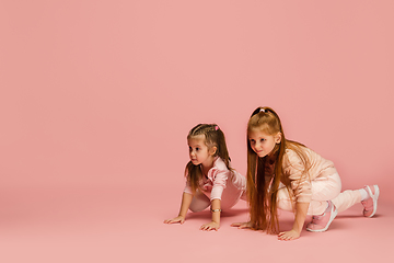 Image showing Happy kids, girls isolated on coral pink studio background. Look happy, cheerful, sincere. Copyspace. Childhood, education, emotions concept