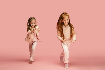 Image showing Happy kids, girls isolated on coral pink studio background. Look happy, cheerful, sincere. Copyspace. Childhood, education, emotions concept