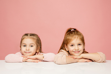 Image showing Happy kids, girls isolated on coral pink studio background. Look happy, cheerful, sincere. Copyspace. Childhood, education, emotions concept