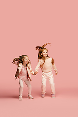 Image showing Happy kids, girls isolated on coral pink studio background. Look happy, cheerful, sincere. Copyspace. Childhood, education, emotions concept