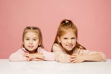 Image showing Happy kids, girls isolated on coral pink studio background. Look happy, cheerful, sincere. Copyspace. Childhood, education, emotions concept