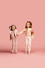 Image showing Happy kids, girls isolated on coral pink studio background. Look happy, cheerful, sincere. Copyspace. Childhood, education, emotions concept