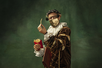 Image showing Portrait of medieval young man in vintage clothing and golden face mask standing on dark background.