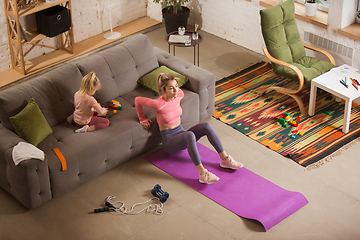 Image showing Young woman exercising fitness, aerobic, yoga at home, sporty lifestyle. Getting active while her child playing on the background, home gym.