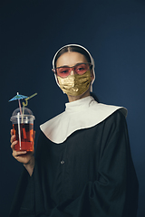 Image showing Medieval young woman as a nun in vintage clothing and golden face mask on dark blue background. Concept of comparison of eras, protection from covid