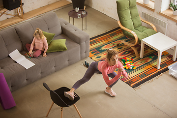 Image showing Young woman exercising fitness, aerobic, yoga at home, sporty lifestyle. Getting active with her child playing, home gym.