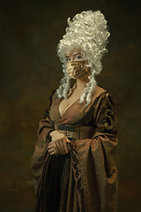 Image showing Portrait of medieval young woman in vintage clothes and golden face mask on dark background.