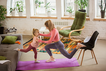 Image showing Young woman exercising fitness, aerobic, yoga at home, sporty lifestyle. Getting active with her child playing, home gym.