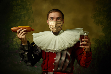 Image showing Portrait of medieval young man in vintage clothing and golden face mask standing on dark background.