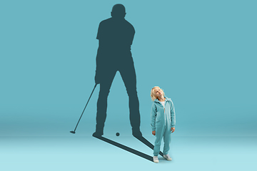 Image showing Childhood and dream about big and famous future. Conceptual image with boy and shadow of fit male golf player on blue background