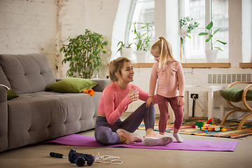 Image showing Young woman exercising fitness, aerobic, yoga at home, sporty lifestyle. Getting active while child, daughter playing with her, home gym.