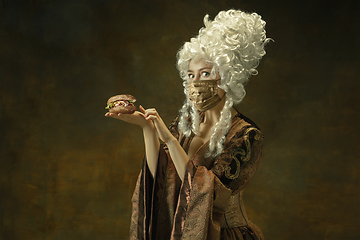 Image showing Portrait of medieval young woman in vintage clothes and golden face mask on dark background.