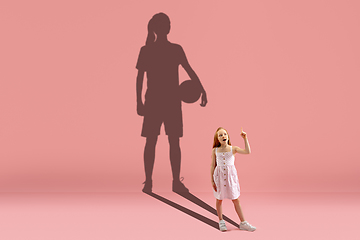 Image showing Childhood and dream about big and famous future. Conceptual image with girl and shadow of fit basketball or soccer female player on coral pink background