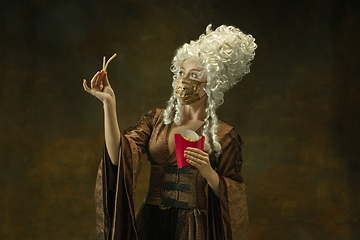 Image showing Portrait of medieval young woman in vintage clothes and golden face mask on dark background.