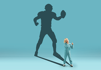 Image showing Childhood and dream about big and famous future. Conceptual image with boy and shadow of fit male american football player on blue background