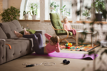 Image showing Young woman exercising fitness, aerobic, yoga at home, sporty lifestyle. Getting active while her child playing on the background, home gym.
