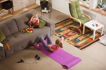 Image showing Young woman exercising fitness, aerobic, yoga at home, sporty lifestyle. Getting active while her child playing on the background, home gym.