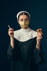 Image showing Medieval young woman as a nun in vintage clothing and golden face mask on dark blue background. Concept of comparison of eras, protection from covid