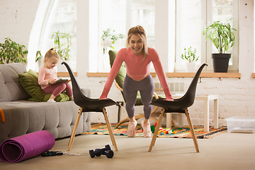 Image showing Young woman exercising fitness, aerobic, yoga at home, sporty lifestyle. Getting active with her child playing, home gym.